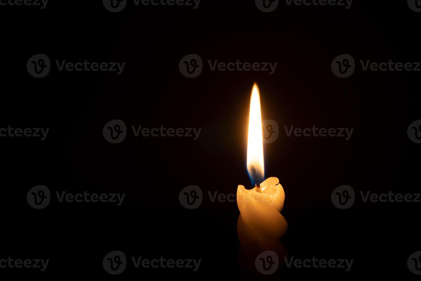 A single burning candle flame or light glowing on a spiral white candle on black or dark background on table in church for Christmas, funeral or memorial service with copy space photo