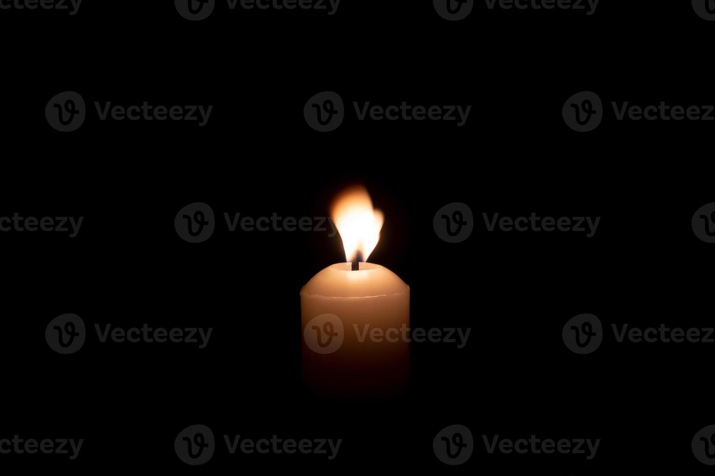 A single candle light glowing on a big white candle against blowing wind on table in church for Christmas, funeral or memorial service with copy space isolated on black background photo