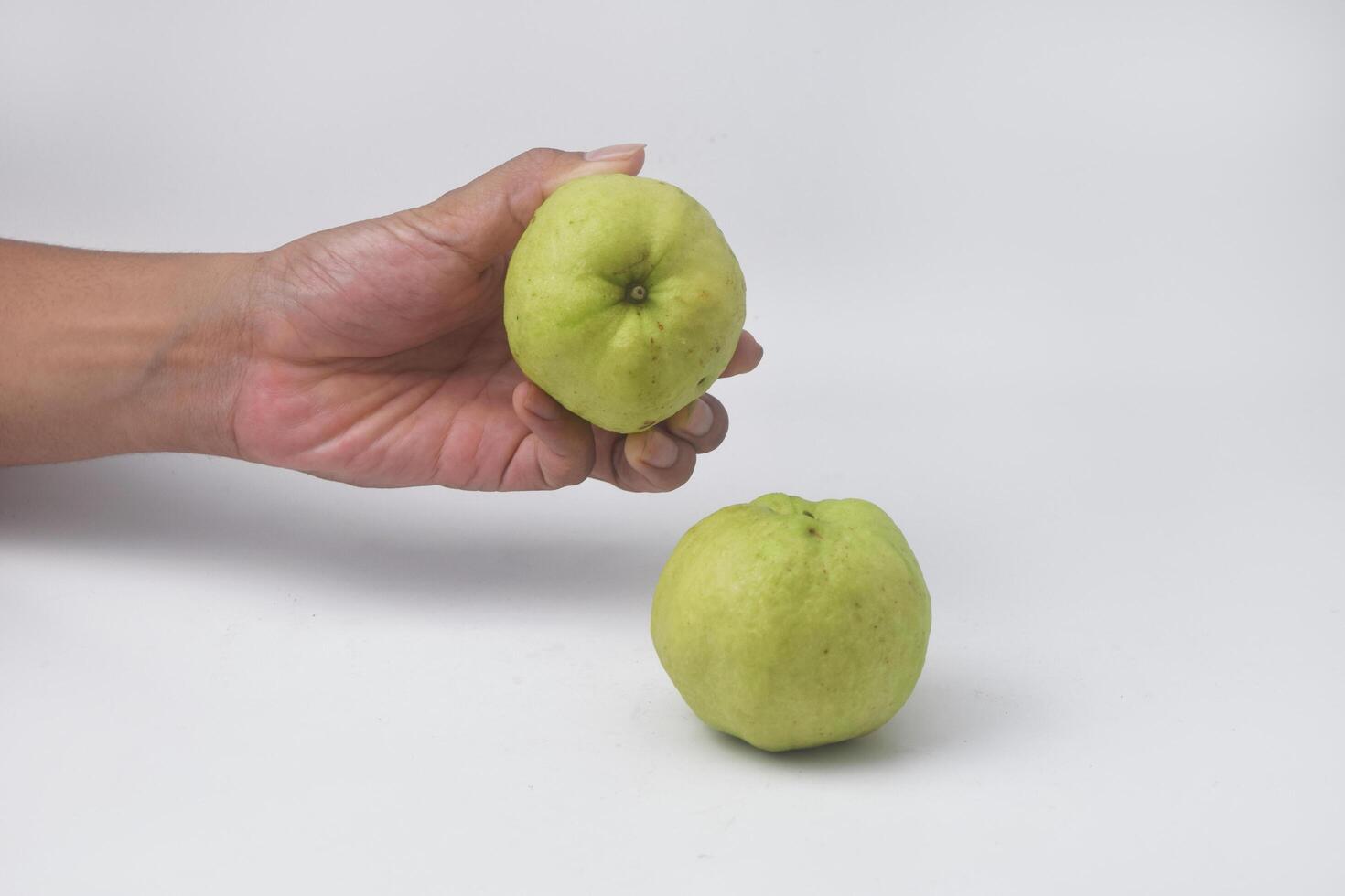 Someones hand is picking up green guavas on an isolated white background photo