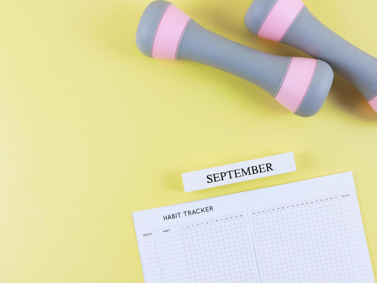 flat lay of habit tracker book, wooden calendar September, gray pink dumbbells, on yellow background with copy space. Self development and active lifestyle concept. photo