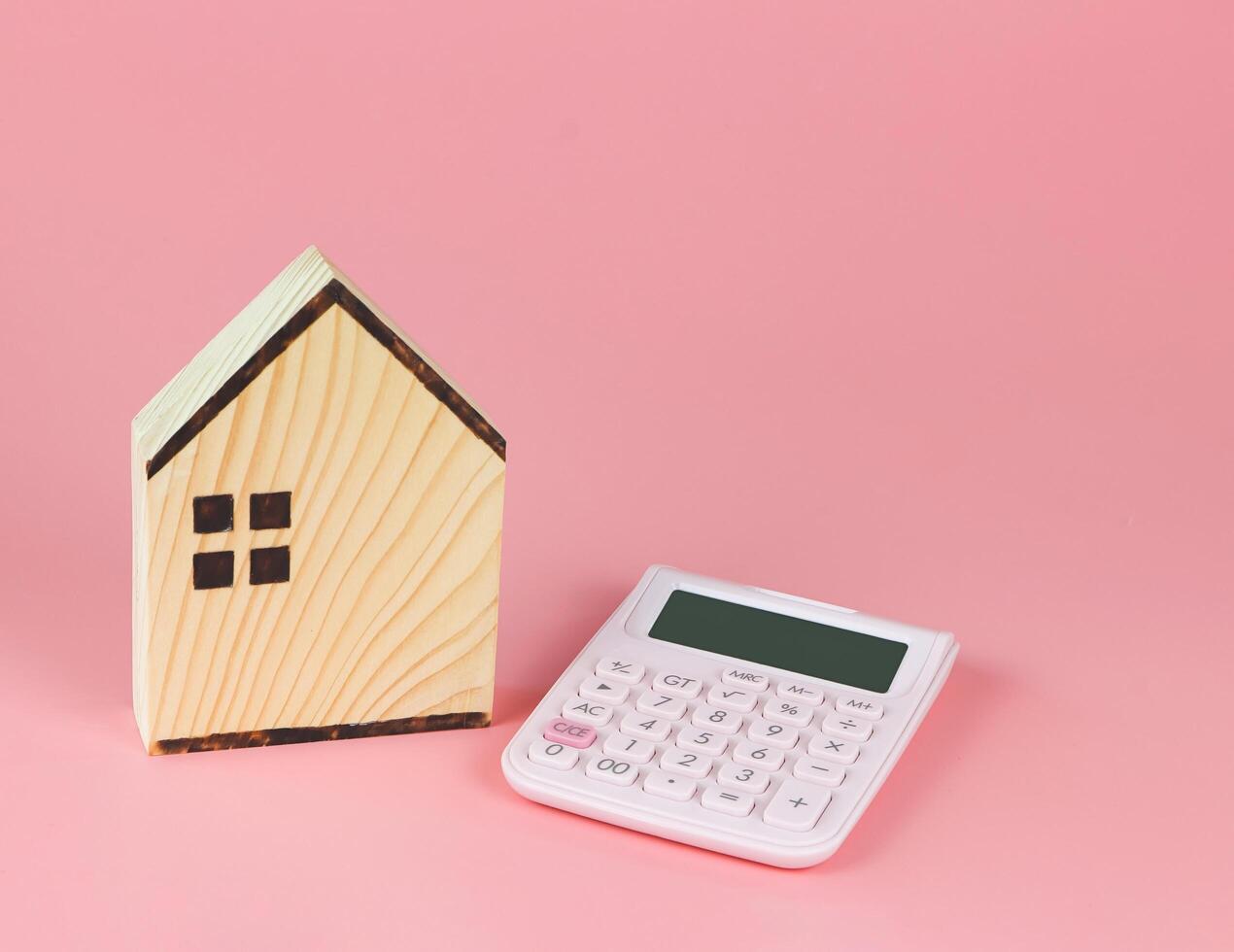 wooden house model and pink calculator on pink background with copy space, home purchase concept. photo