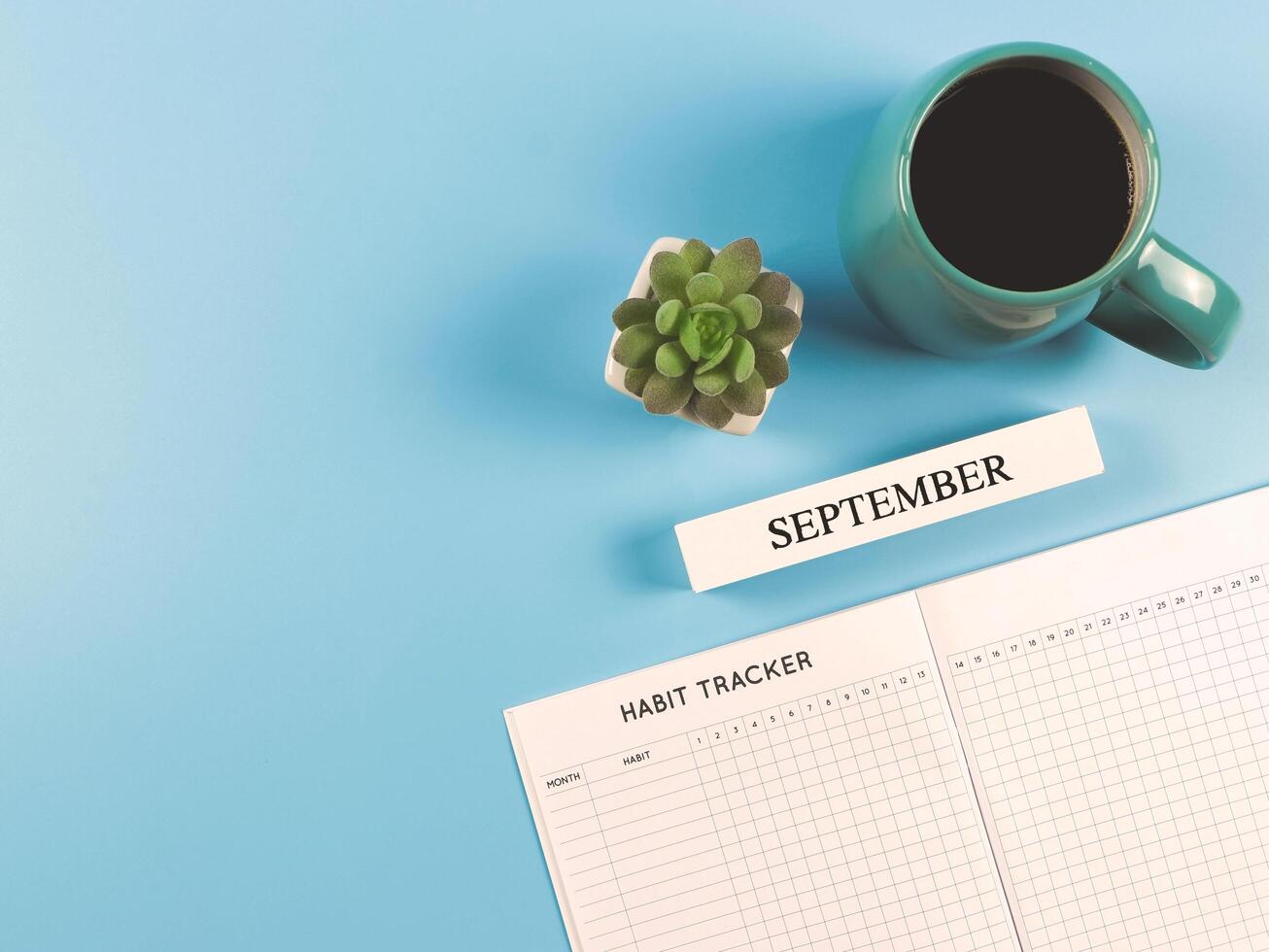 flat lay of habit tracker book with wooden calendar September, blue cup of black coffee and succulent plant pot on blue background with copy space. photo