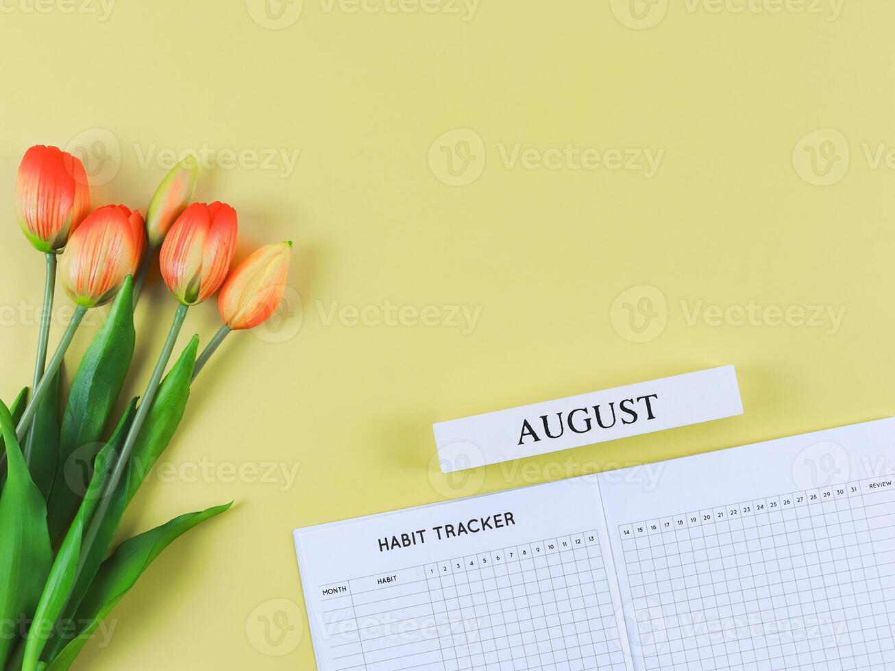 flat lay of habit tracker book with wooden calendar August, and tulips on yellow background. Copy space. photo
