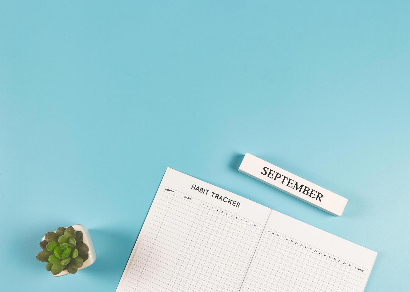flat lay of habit tracker book with succulent plant pot and wooden calendar September on blue background with copy space. photo