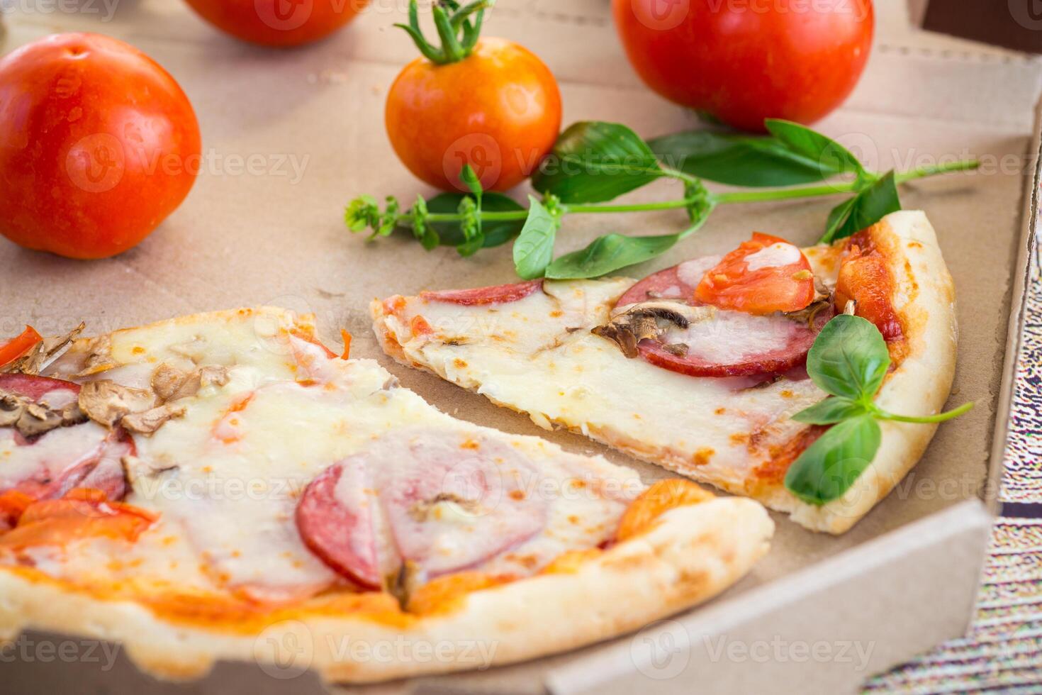 cooked pizza with salami and sausage in a box on a wooden table photo