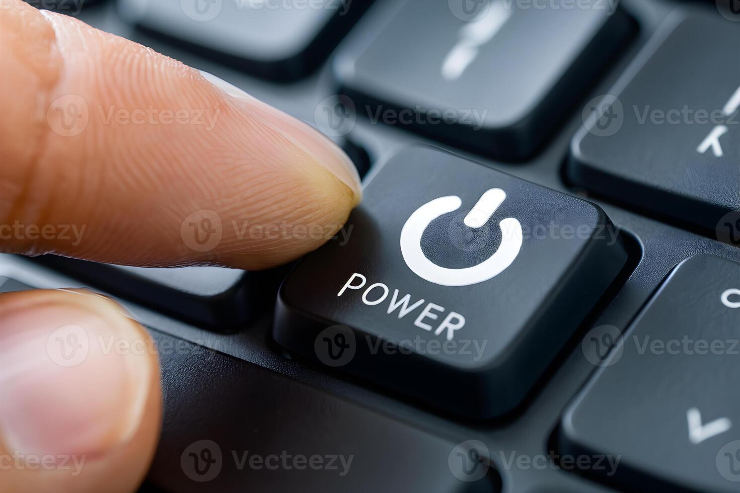 Finger presses black power button on keyboard, white power icon, blurred keys photo