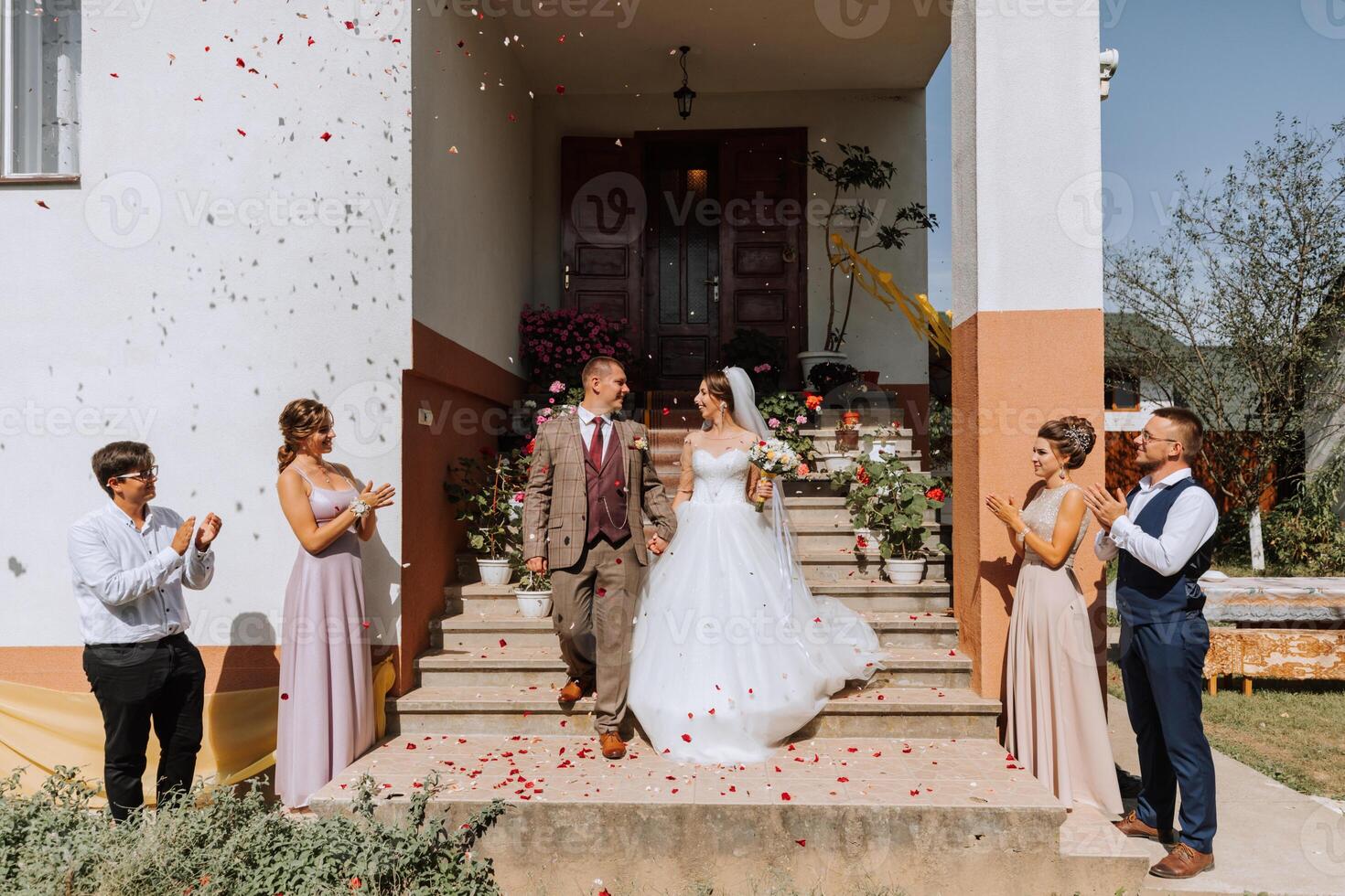 A bride and groom are walking down the stairs of a house, with a group of people watching them photo