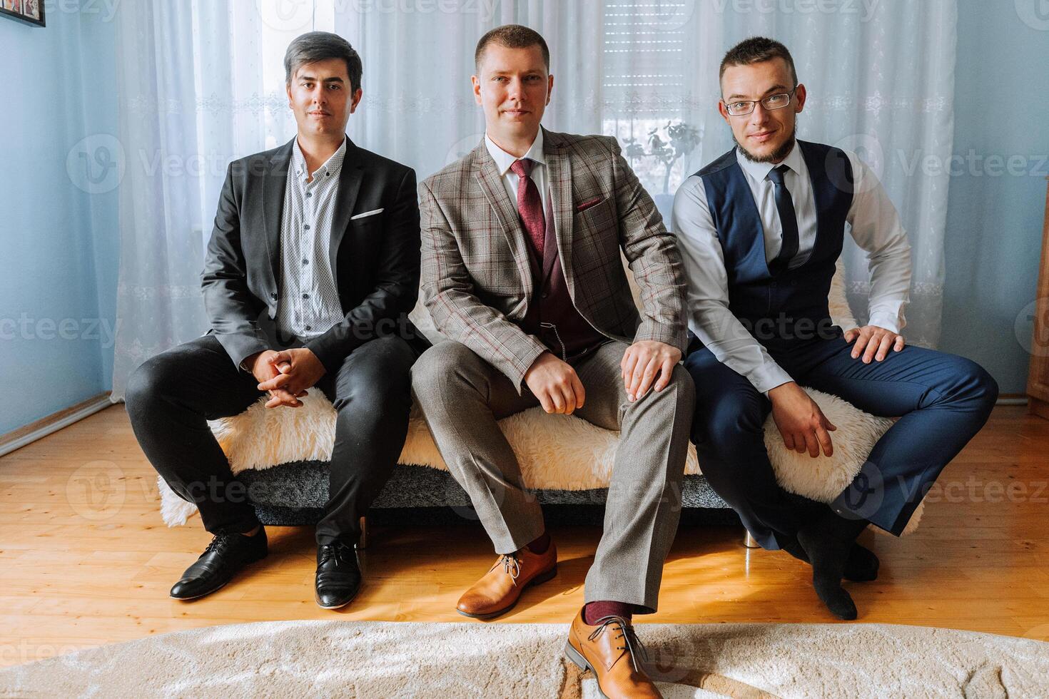 Three men in suits are sitting on a couch. They are all wearing ties and are posing for a picture. Scene is formal and professional photo