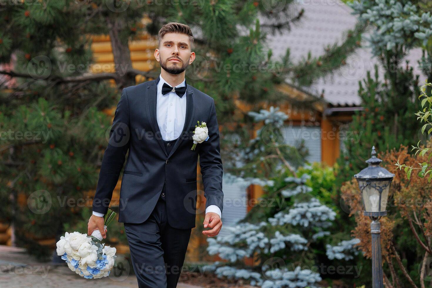A man in a suit and tie is walking down a path with a bouquet of flowers in his hand photo