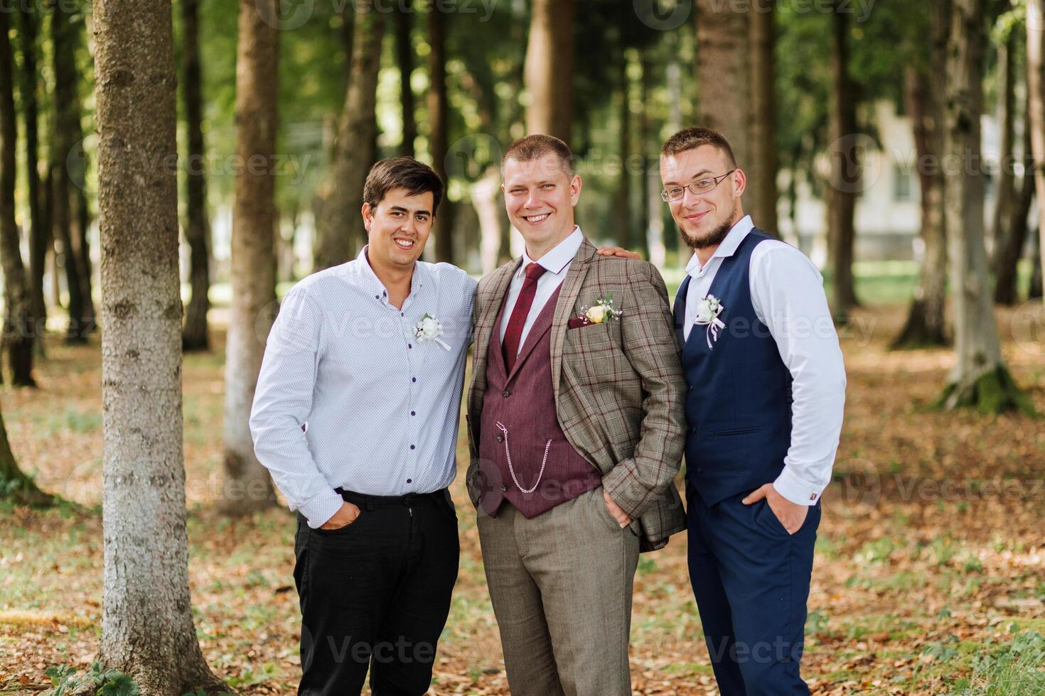 Three men are standing in a forest, one of them wearing a tie. They are smiling and posing for a picture photo