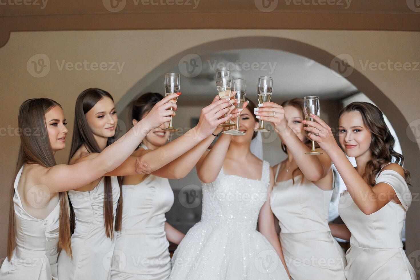 A group of women are celebrating a wedding, with one of them holding a glass of champagne. The bride is in the center of the group, surrounded by her bridesmaids. Scene is joyful and celebratory photo