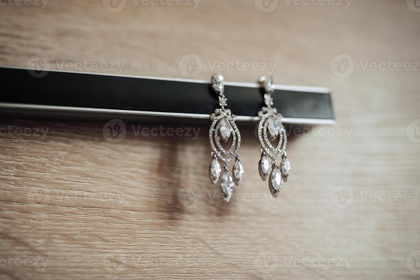 A pair of earrings with a diamond design are sitting on a wooden surface. The earrings are large and shiny, and they appear to be a statement piece. The wooden surface adds a rustic photo