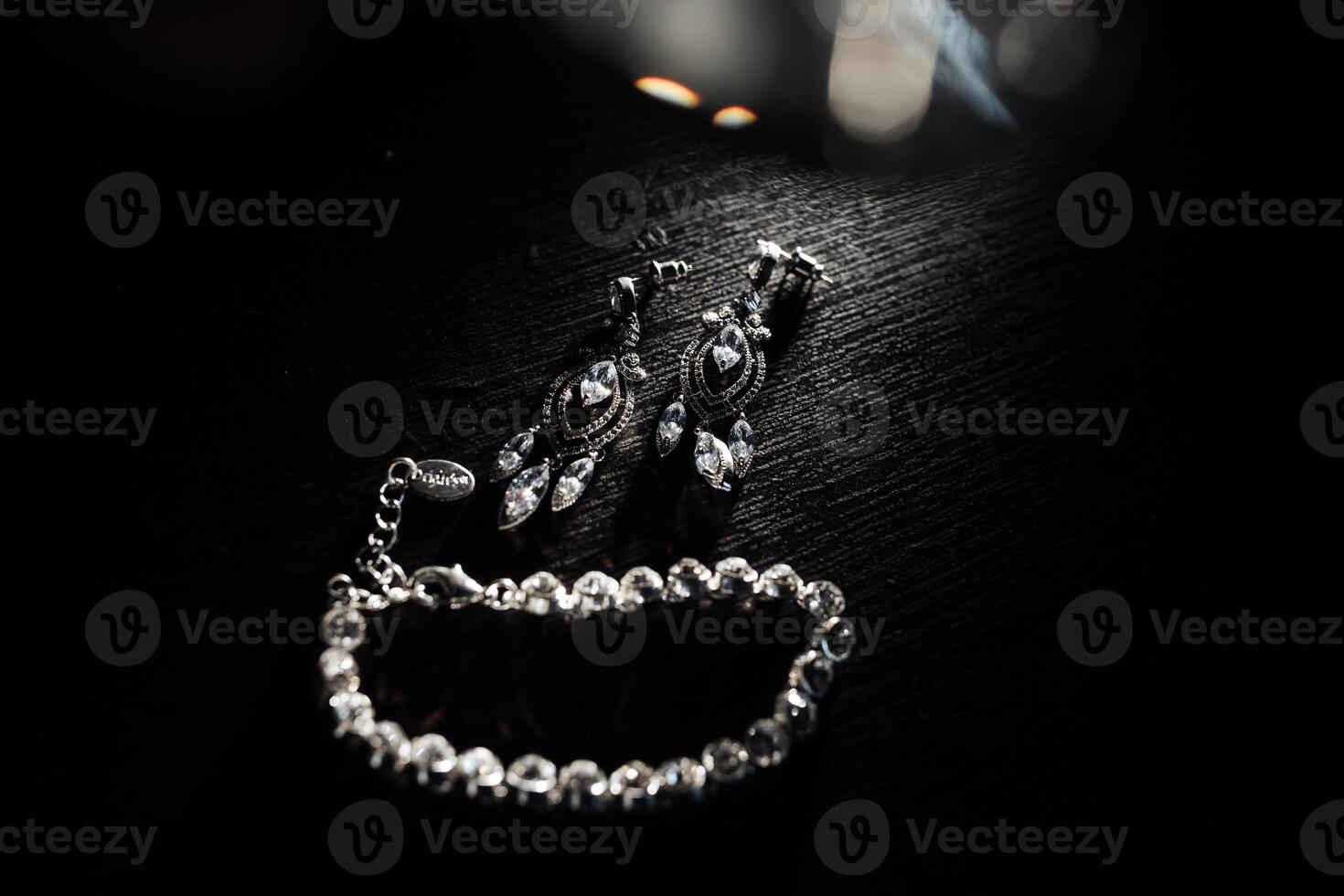 A pair of earrings and a bracelet are displayed on a dark table. The earrings are large and shiny, while the bracelet is smaller and more delicate. Scene is elegant and sophisticated photo