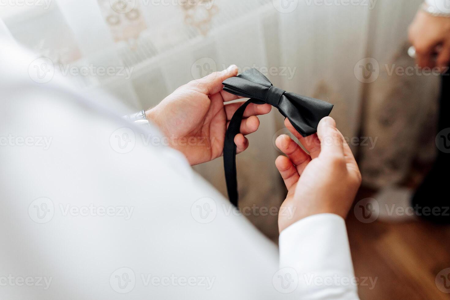 A man is getting ready for a formal event and is adjusting his black bow tie. Concept of elegance and sophistication, as the man carefully prepares himself for the occasion photo