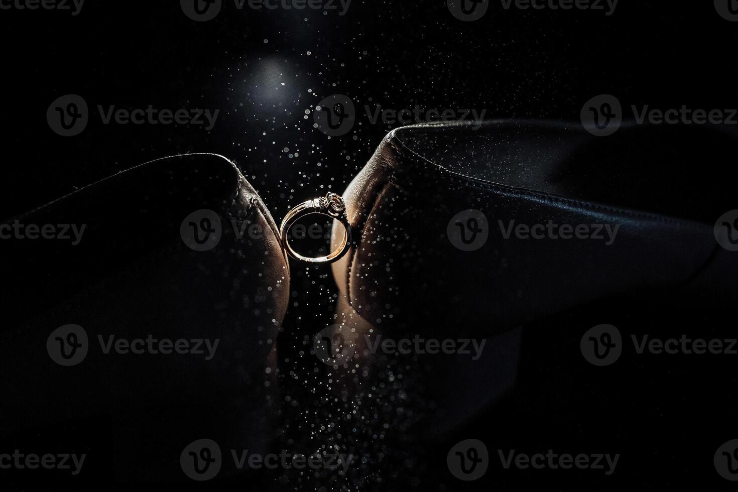 A ring is being shown in a dark room. The ring is gold and is being held by a person. Scene is romantic and intimate photo