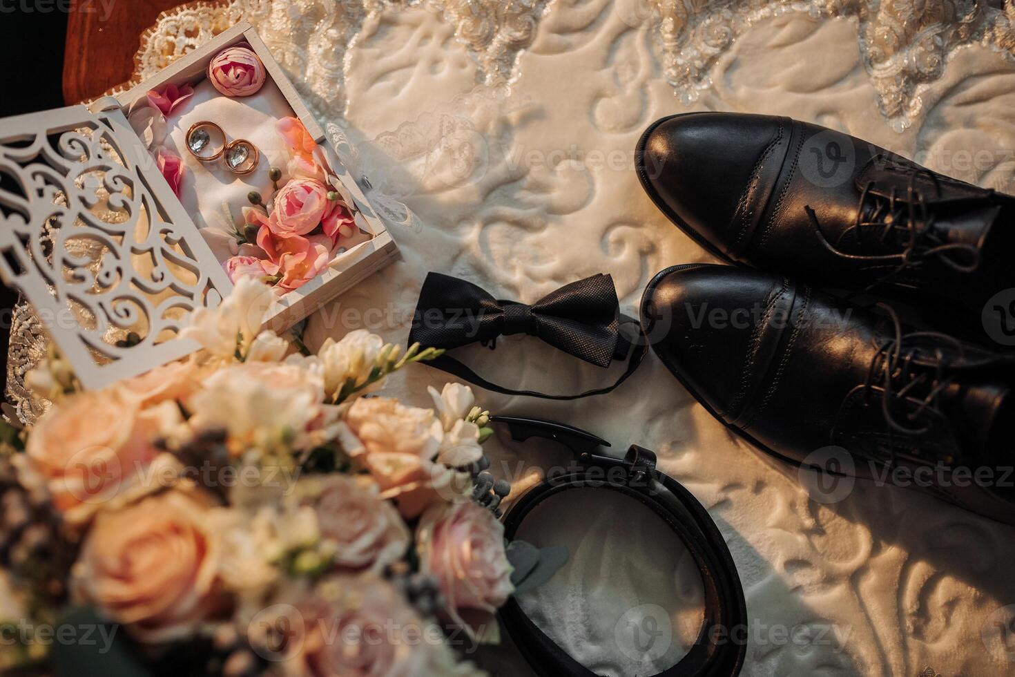 A man's wedding attire is displayed on a table, including a pair of black shoes and a bow tie photo
