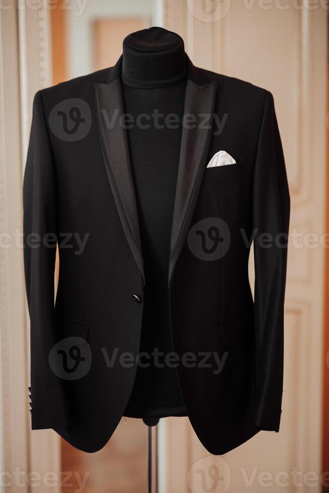 A man in a black suit is wearing a black tie and a white handkerchief. The man is standing in front of a mirror photo
