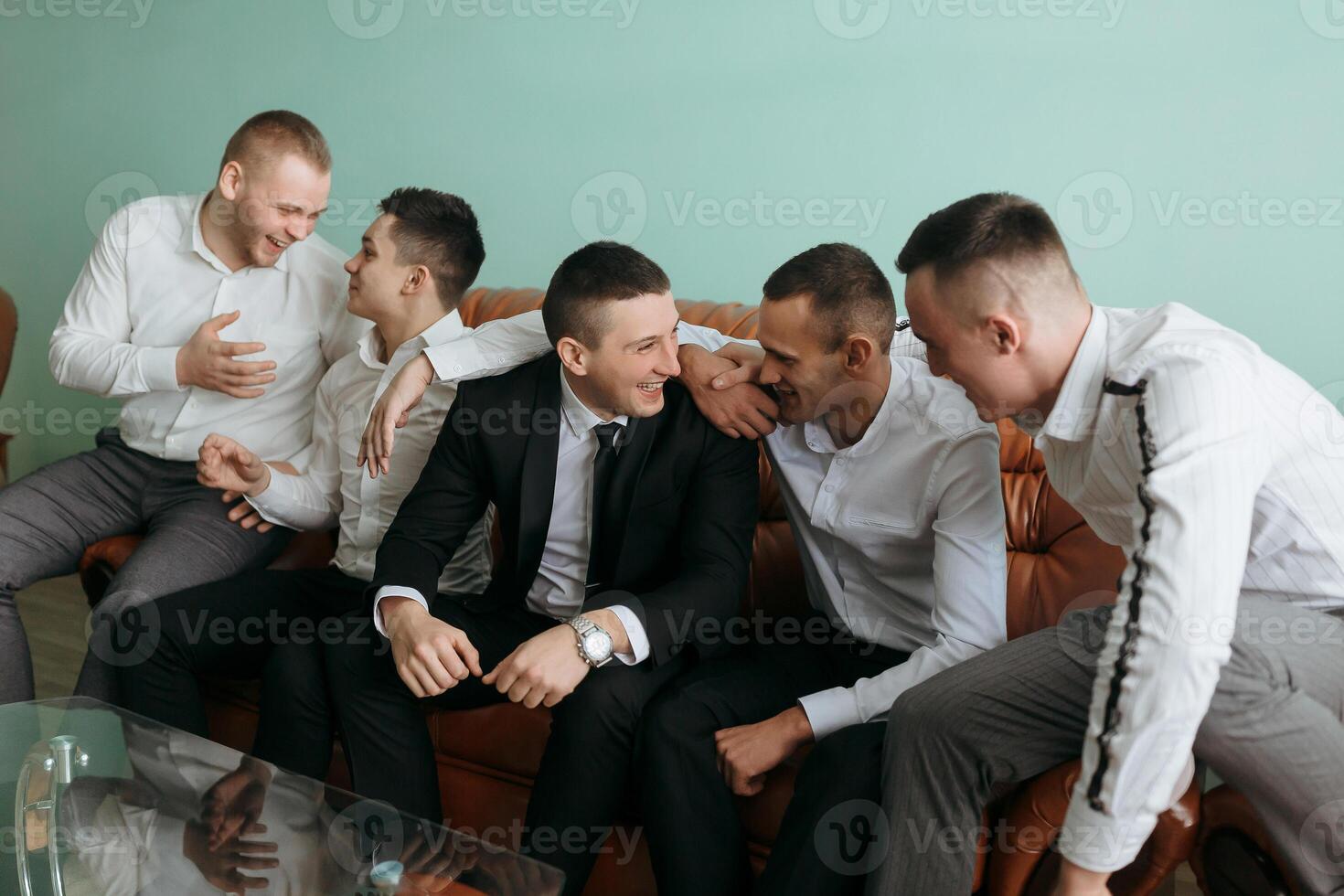 A group of men are sitting on a couch, laughing and hugging each other. Scene is happy and friendly photo
