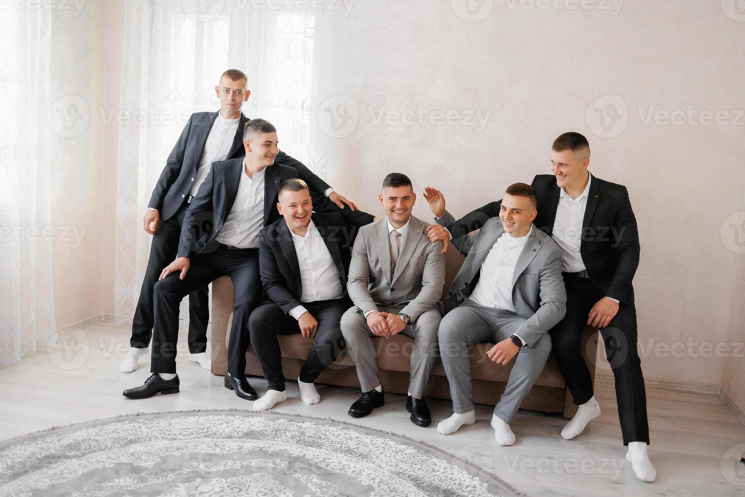 A group of men in suits are sitting on a couch. They are all smiling and seem to be enjoying each other's company photo