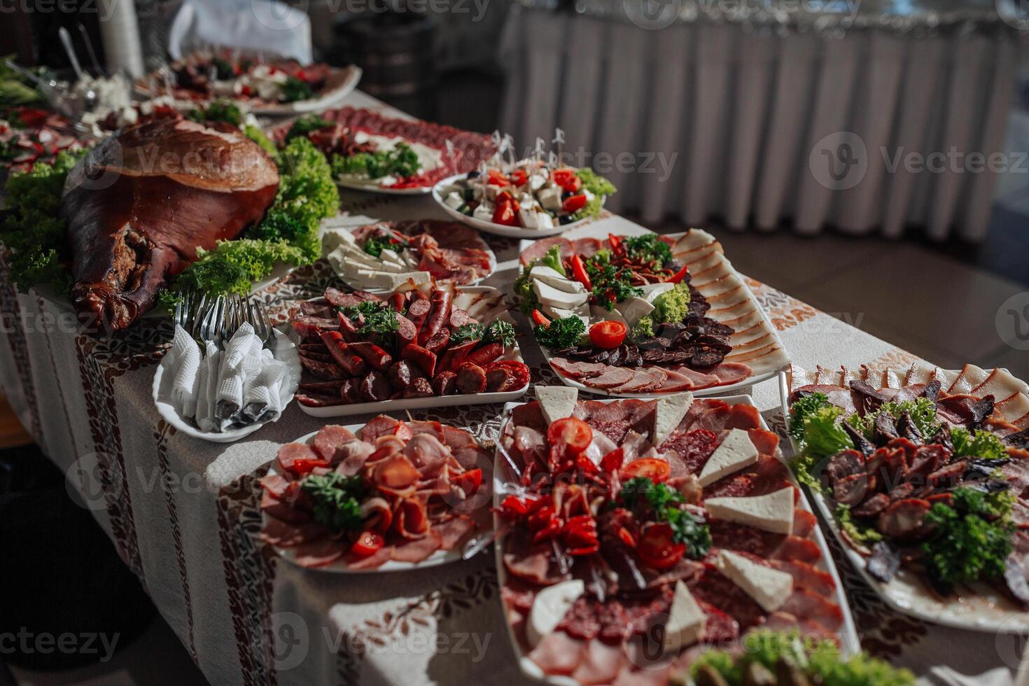 A table is covered with a variety of meats and vegetables, including a large piece of ham. The table is set for a party or gathering, and the food is arranged in an appetizing manner photo