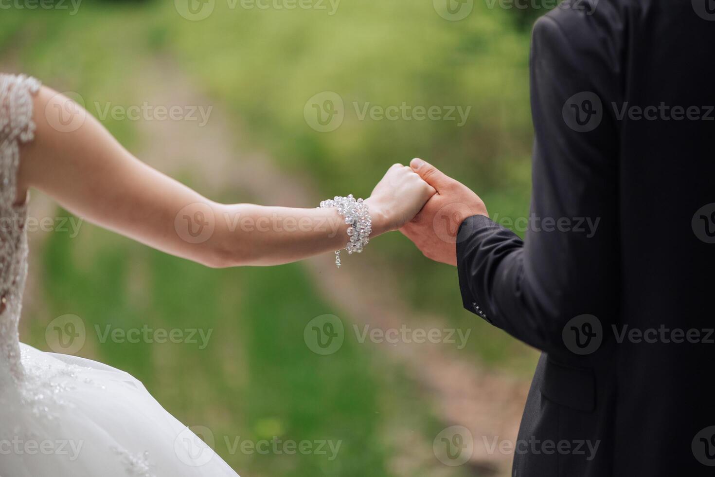 A bride and groom are holding hands in a field. The bride is wearing a white dress and the groom is wearing a black suit. Scene is romantic and happy photo