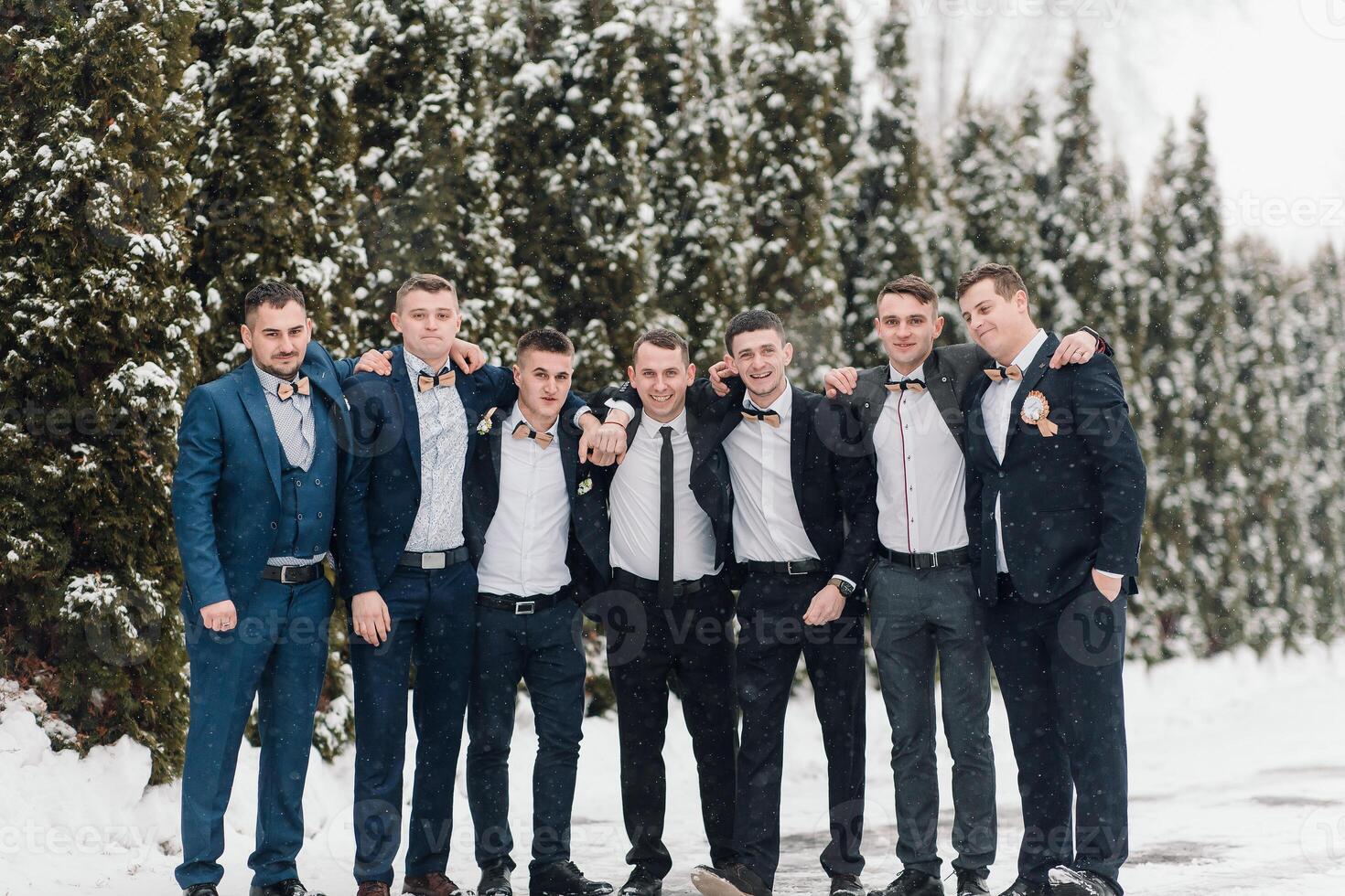 A group of men in suits are posing for a picture in the snow. Scene is festive and celebratory, as the men are dressed in formal attire and appear to be enjoying the winter weather photo