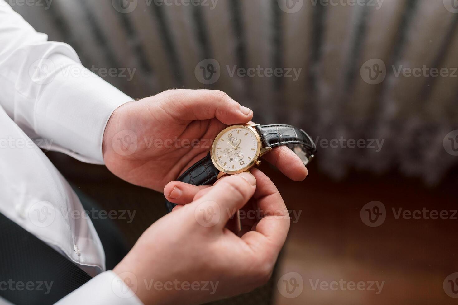 A man is holding a watch in his hand. The watch is black and gold. The man is wearing a white shirt photo