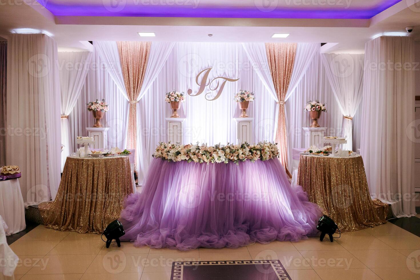 A wedding reception with a purple table and gold tablecloths. The table is decorated with flowers and the room is lit with purple lights photo