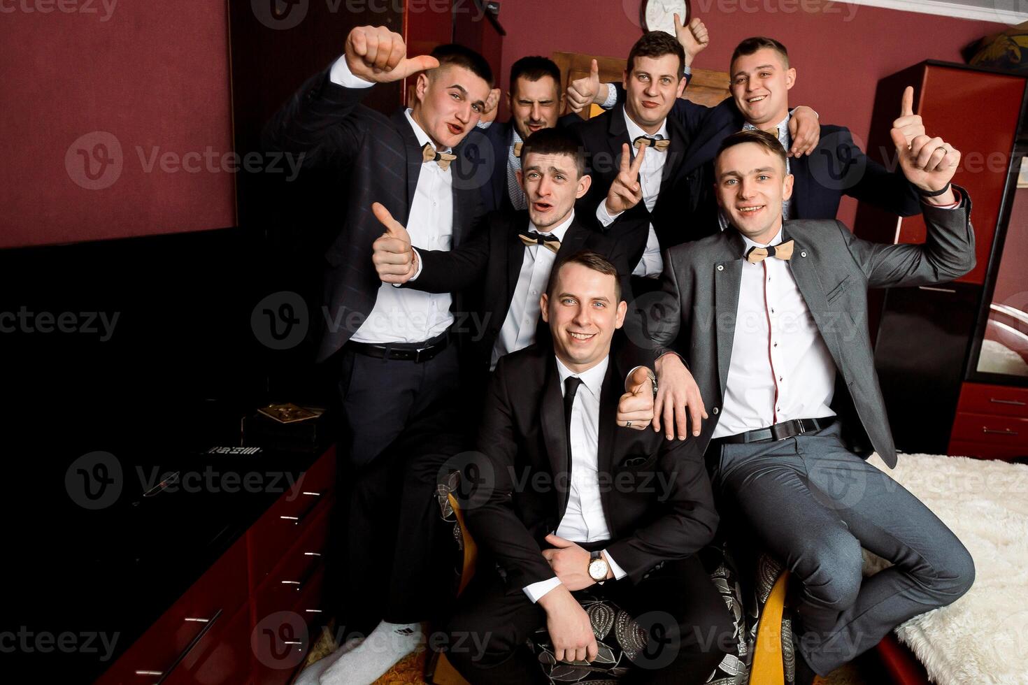 A group of men in suits are posing for a picture, with one man giving a thumbs up. Scene is celebratory and happy, as the men are dressed up and posing for a photo together