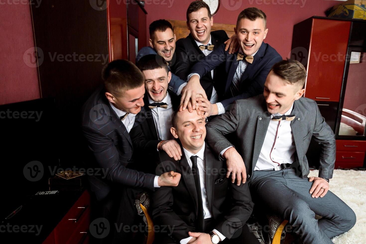 A group of men are posing for a picture, all wearing suits and ties. They are all smiling and seem to be enjoying each other's company. Scene is lighthearted and fun photo
