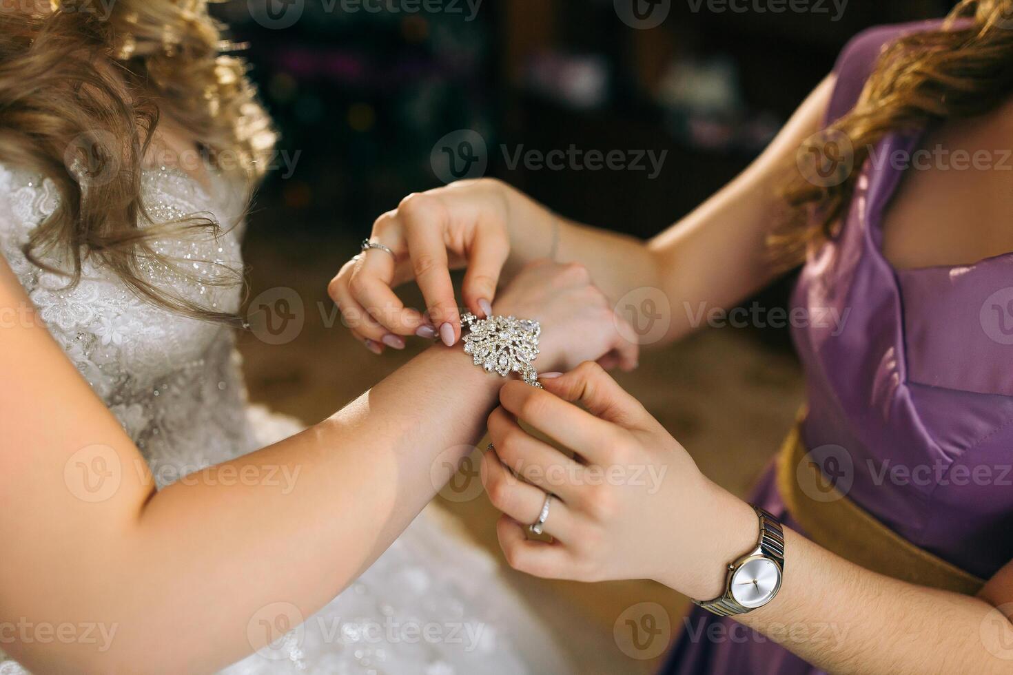 A woman is putting a bracelet on another woman's wrist. The woman on the left is wearing a wedding dress photo