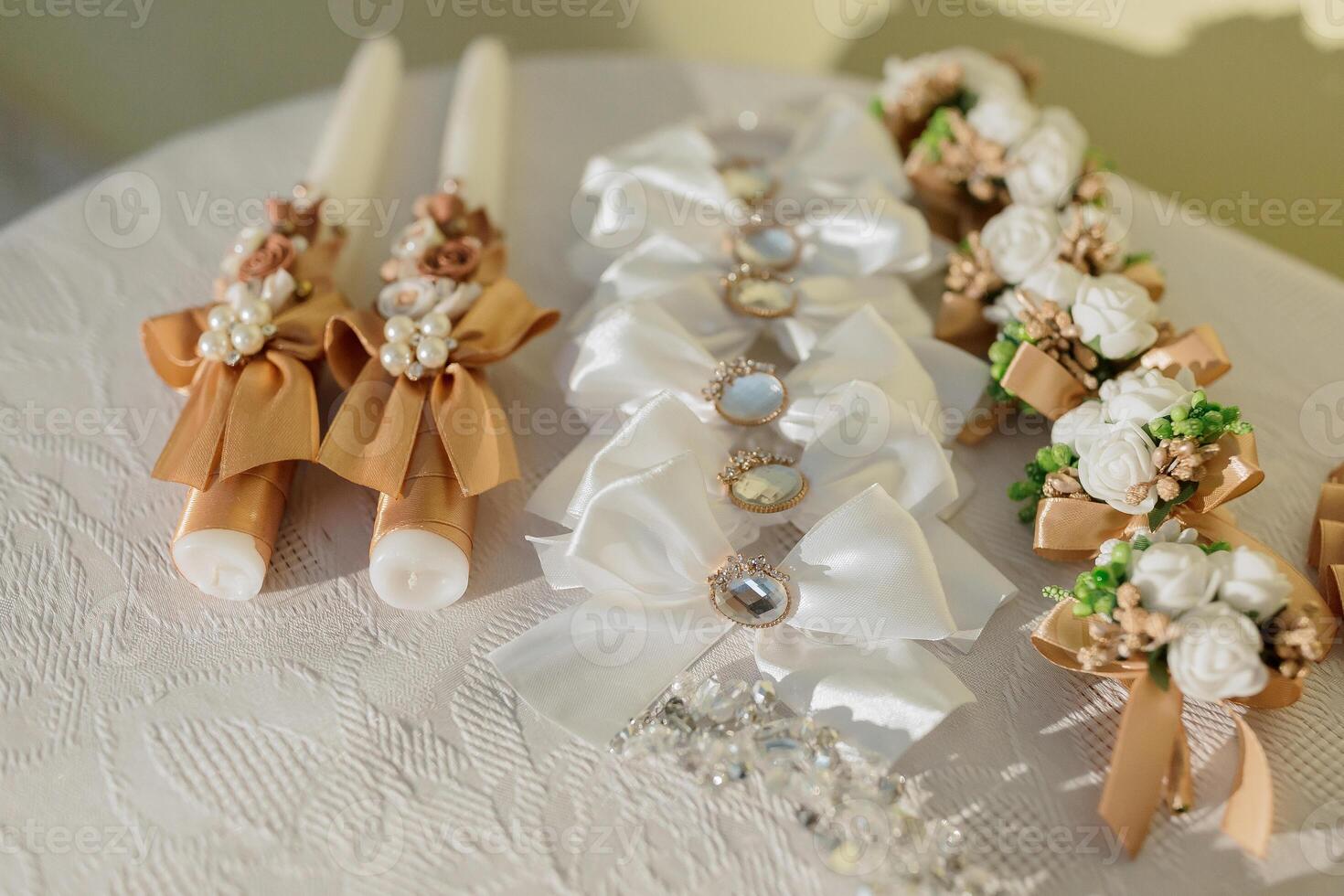 A table with candles and flowers. The candles are in different sizes and colors. The table is white and has a floral pattern photo