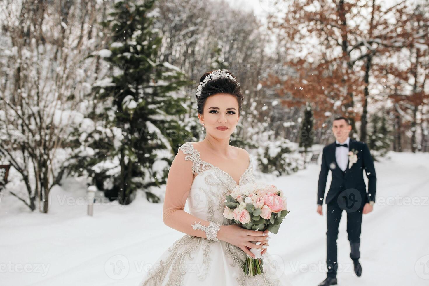 A bride and groom are walking in the snow, the bride is holding a bouquet of flowers photo