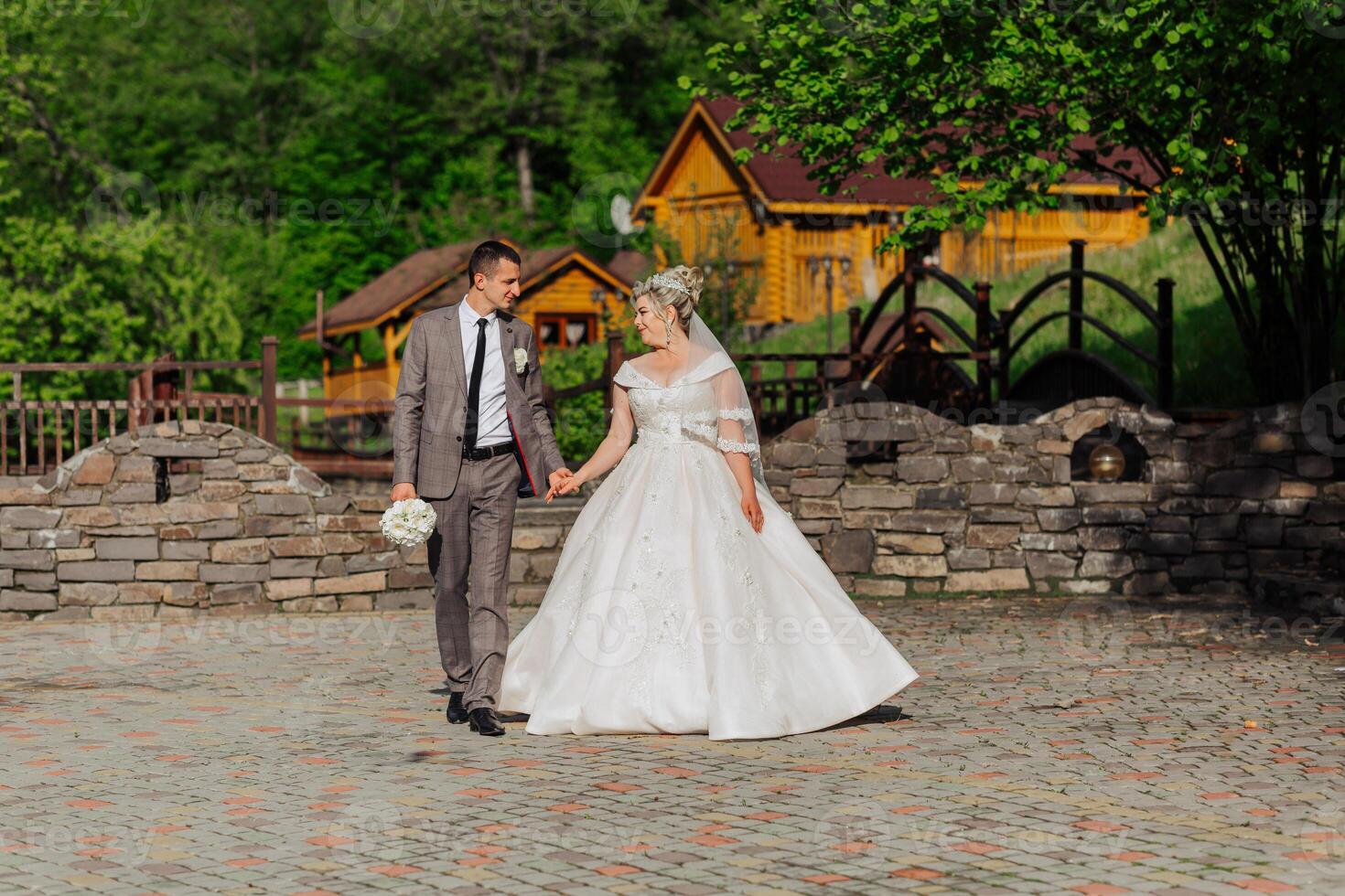 A bride and groom are walking down a path in front of a house. The bride is wearing a white dress and the groom is wearing a suit photo