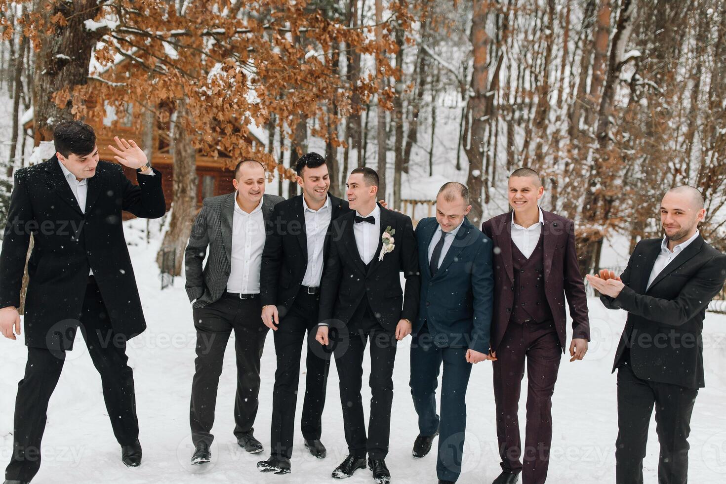 A group of men in suits are posing for a picture in the snow. Scene is lighthearted and festive, as the men are dressed up and enjoying the winter weather photo