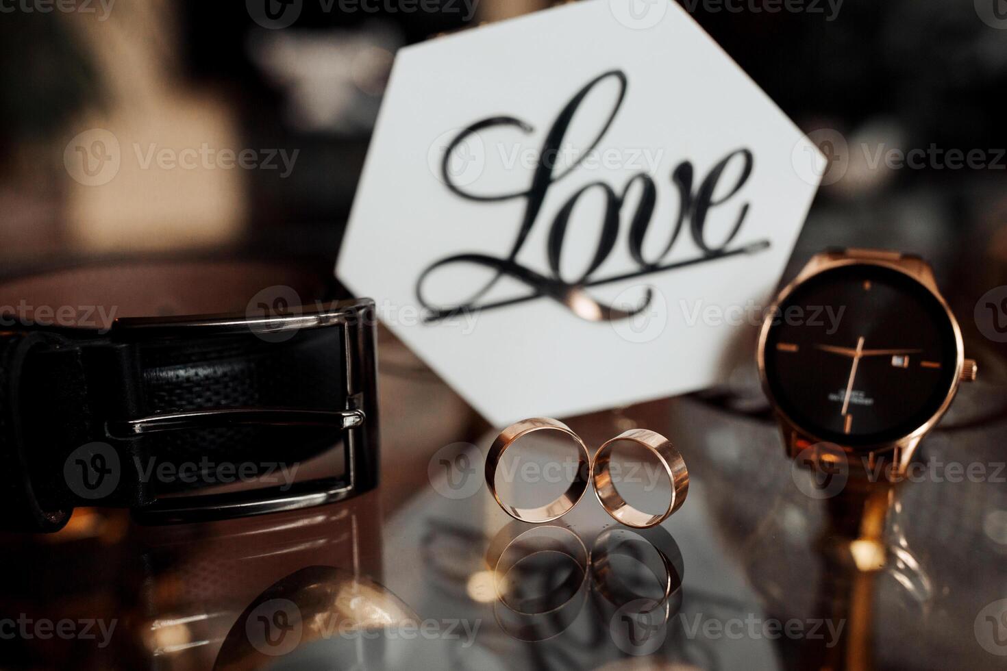 A watch, a ring and a belt are displayed on a table. The watch is a gold watch with a black band photo