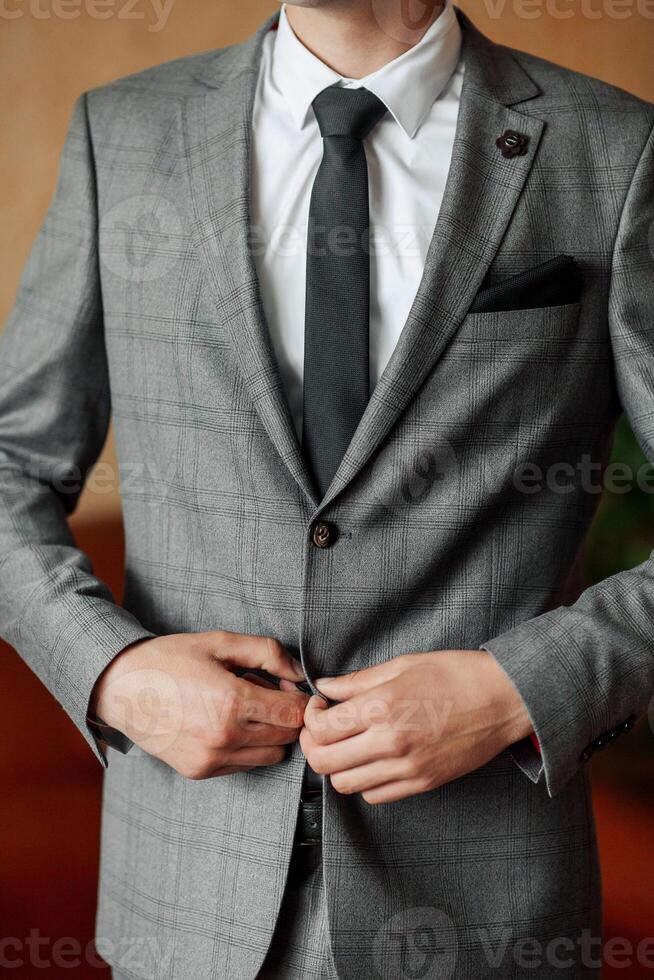 A man in a gray suit and white shirt is adjusting his tie. Concept of formality and professionalism, as the man is dressed in a suit and tie, which is typically worn for business or formal occasions photo