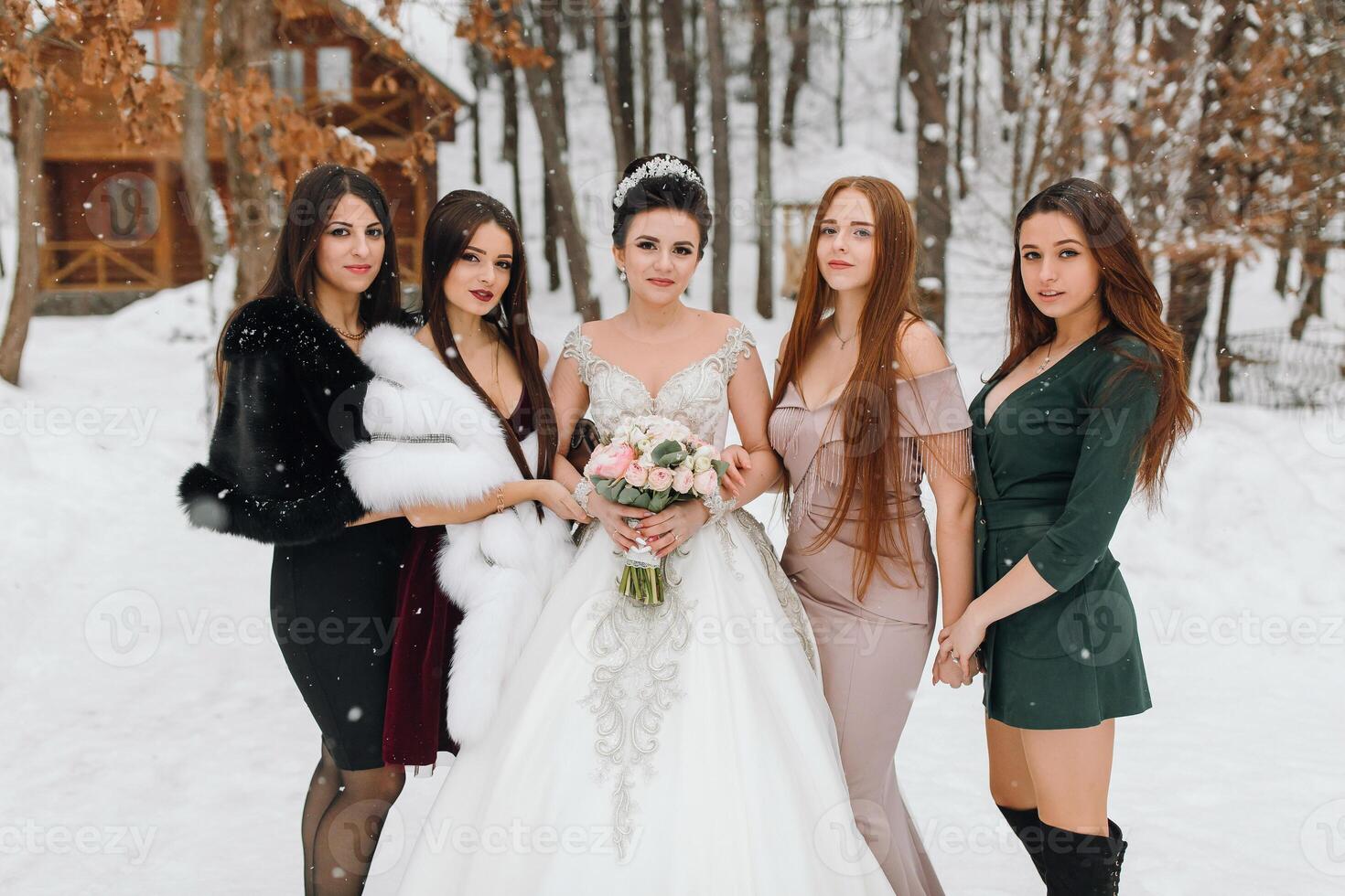 A group of women posing for a picture in the snow, one of them is wearing a white dress and holding a bouquet photo