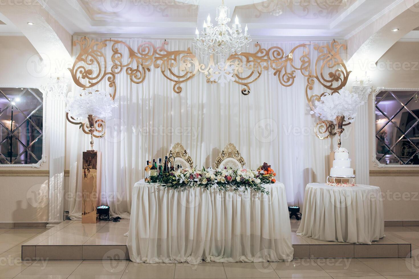 A large white table with a chandelier above it and a cake on it photo