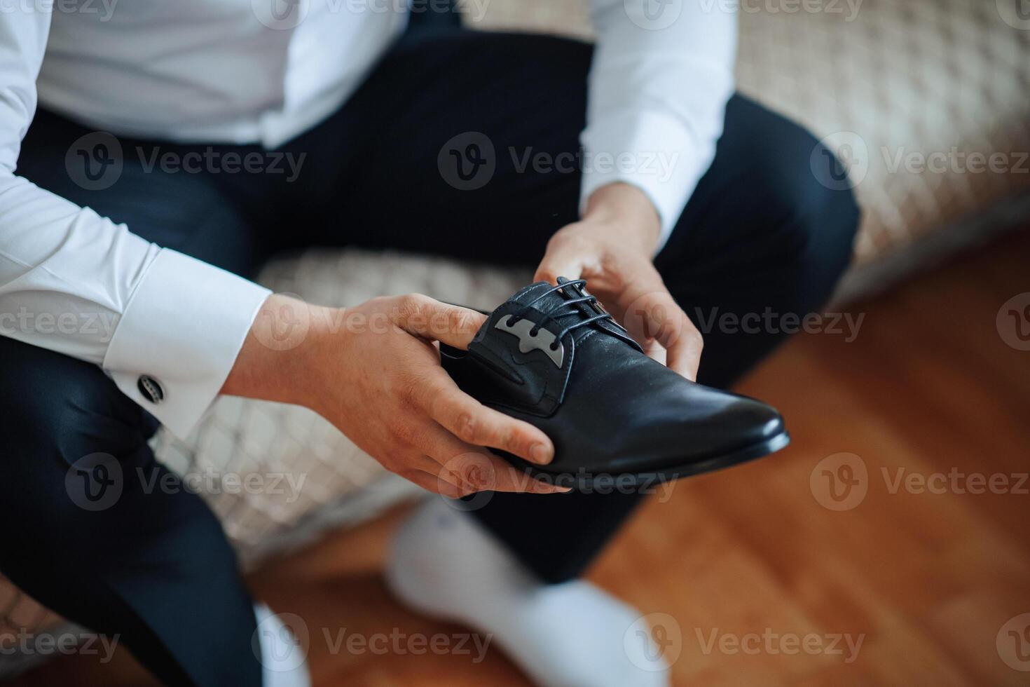 A man is sitting on a couch and holding a black shoe. He is wearing a suit and tie photo
