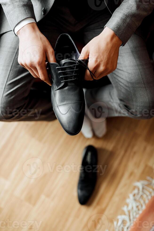A man is putting on a black shoe. The shoe is on a wooden floor. The man is wearing a suit photo