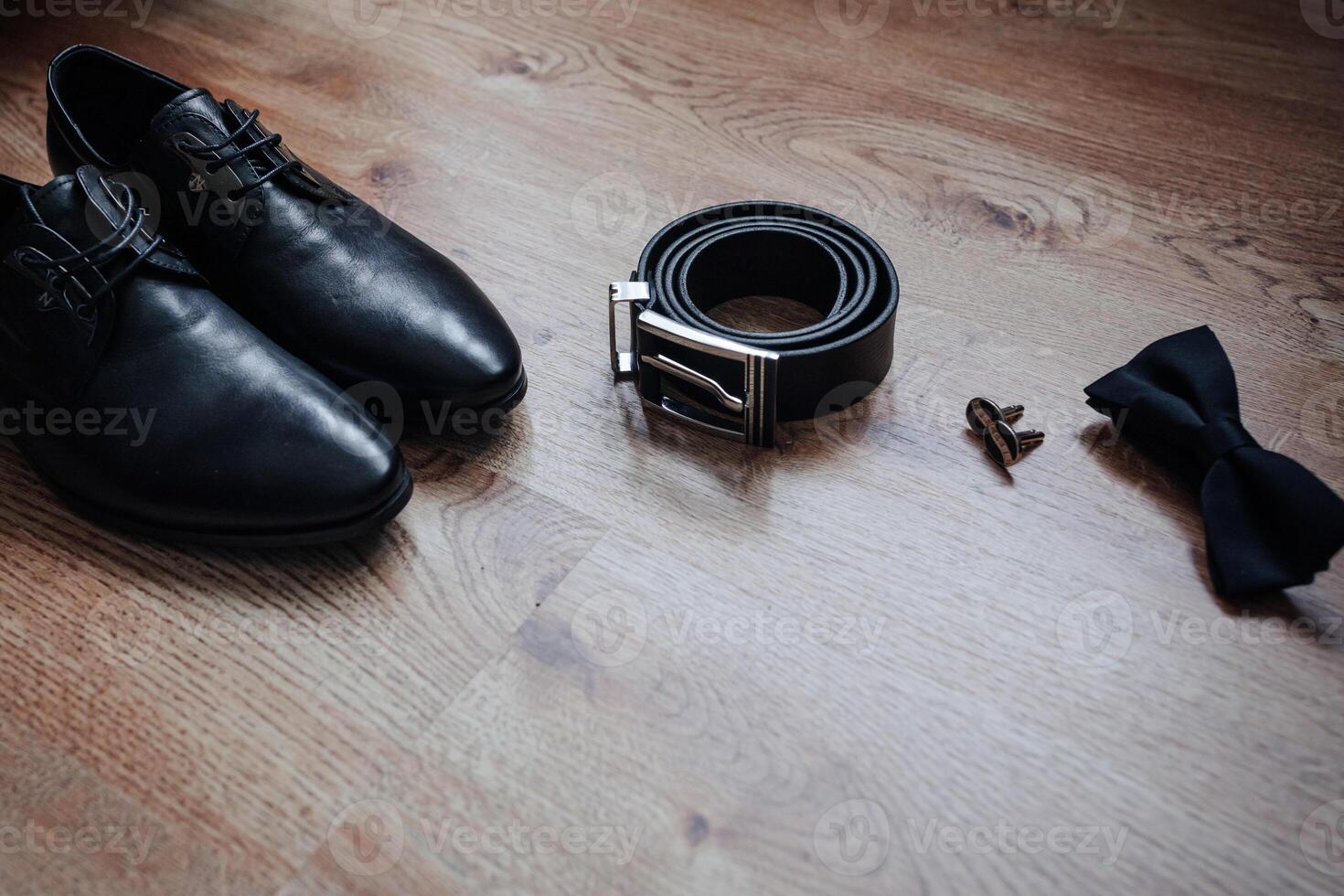 A pair of shoes and a belt are laid out on a wooden floor. The shoes are black and the belt is black as well photo