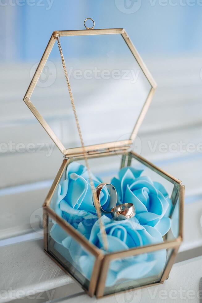 A gold and blue box with a blue rose and two gold rings inside. The box is placed on a table photo