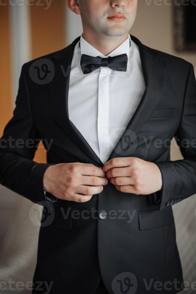 A man in a black suit and white shirt is getting ready to tie his bow tie. Concept of formality and elegance, as the man is dressed in a tuxedo and preparing for a special occasion photo