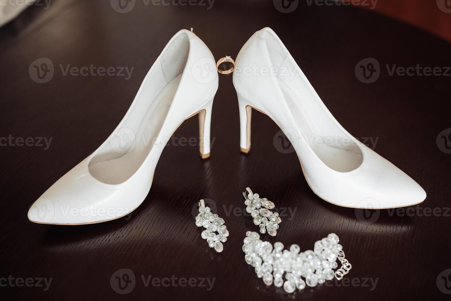 A pair of white shoes with a ring on the back and a pair of pearl earrings. The shoes are placed on a table with a black background photo