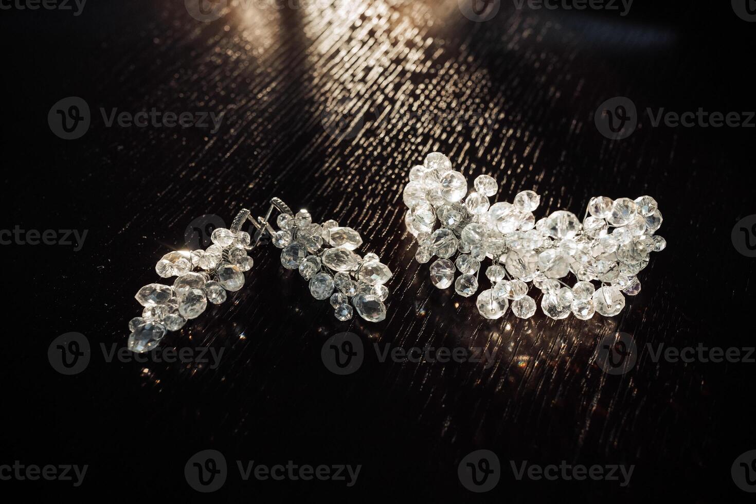 A pair of earrings and a bracelet are displayed on a dark table. The earrings are large and have a lot of detail, while the bracelet is smaller and has a more delicate design photo