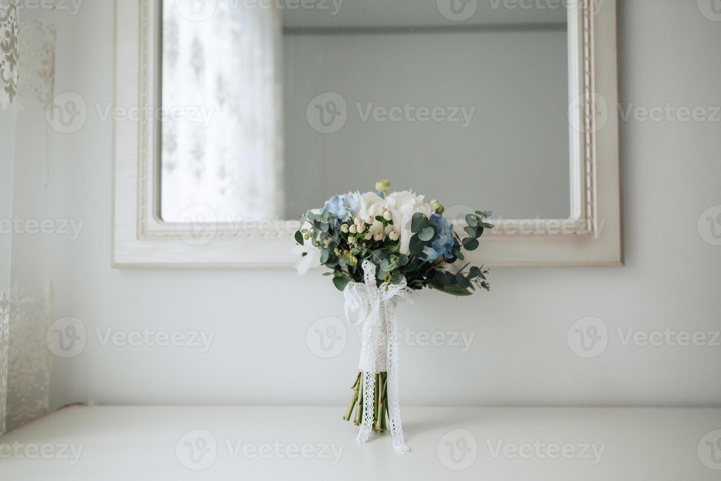 A bouquet of flowers sits on a table in front of a mirror. The flowers are blue and white, and the arrangement is simple and elegant. The mirror reflects the flowers, creating a sense of depth photo