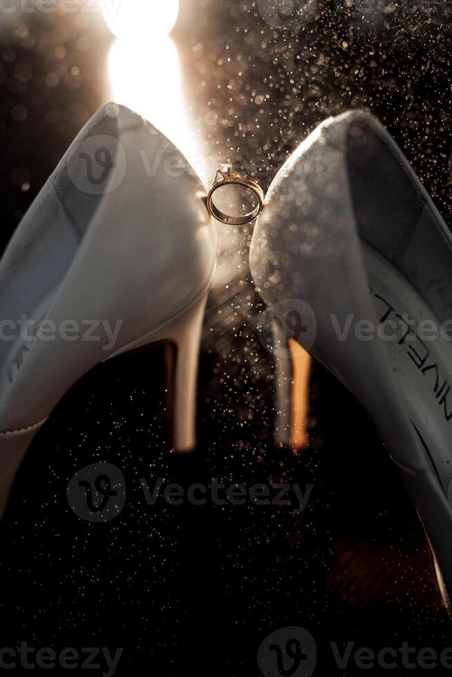 A pair of white shoes with a ring on the left shoe. The shoes are covered in glitter and the ring is shining photo