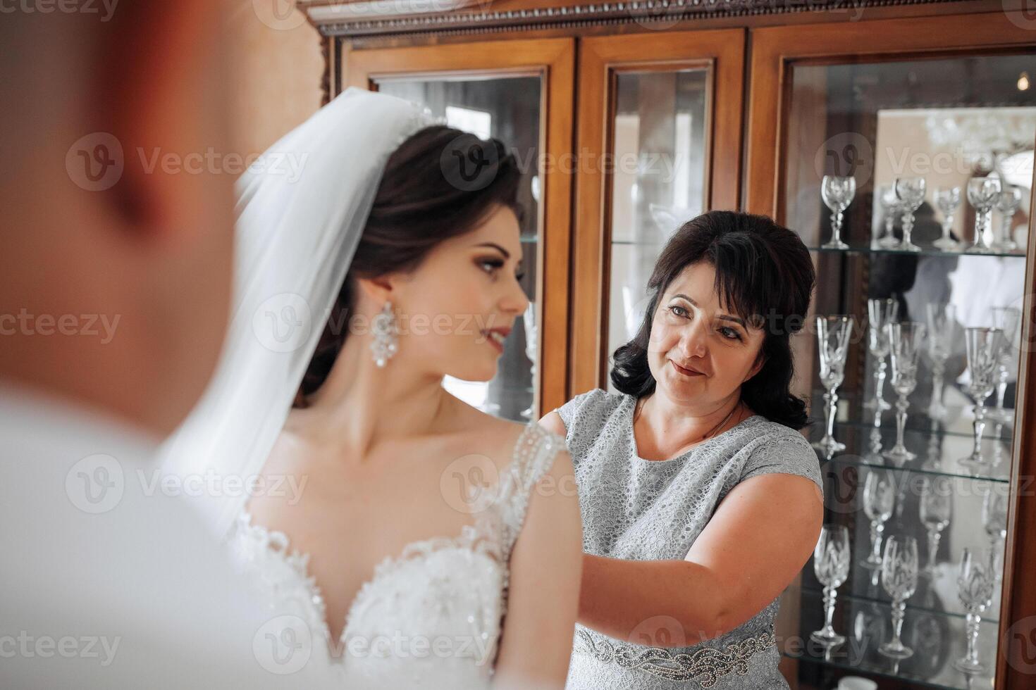 A bride is getting ready for her wedding and her mother is helping her. Scene is one of love and support between the two women photo