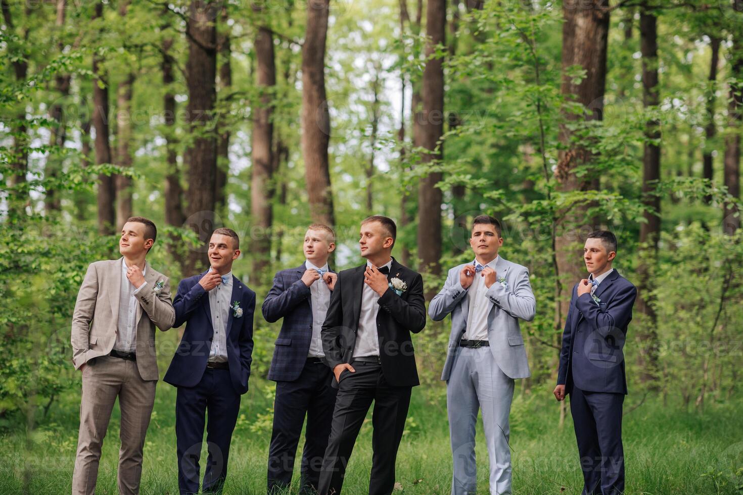 A group of men in suits are standing in a forest. They are all dressed up and looking at something photo